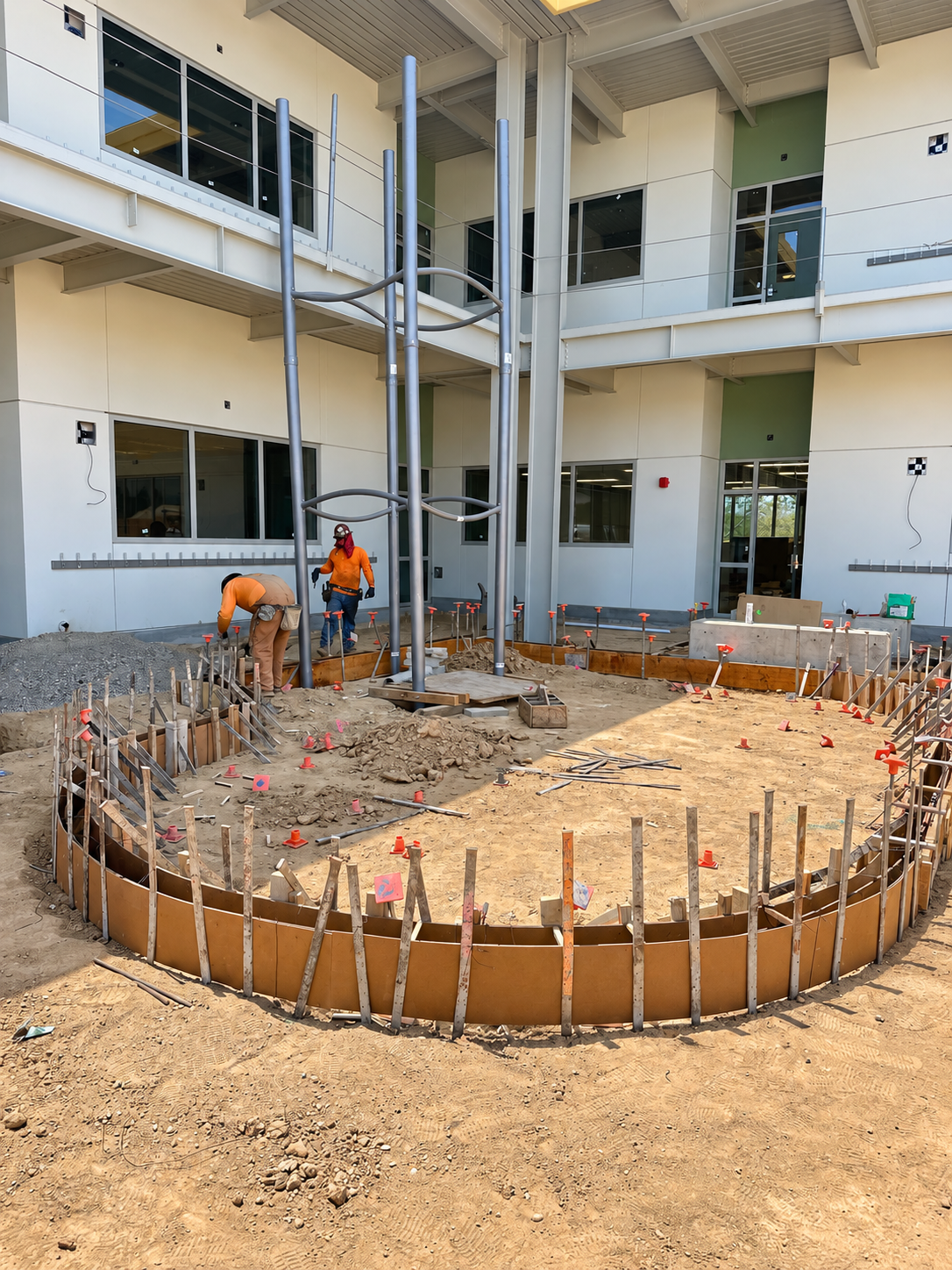 Workers preparing curved concrete formwork in a school courtyard